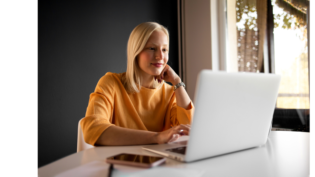 Blonde Frau mit orangenem Pullover sitzt vor ihrem Laptop