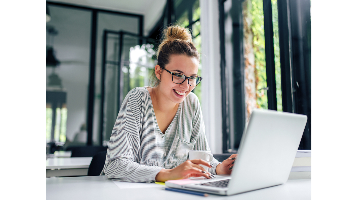 Frau mit Brille sitzt am Laptop und lächelt