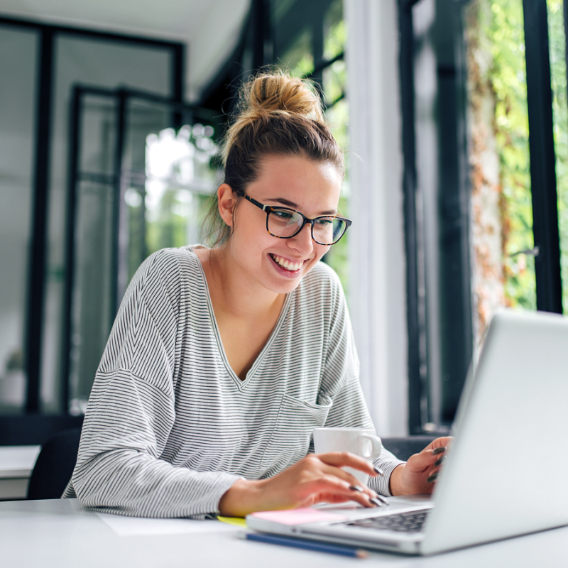 Frau mit Brille sitzt am Laptop und lächelt