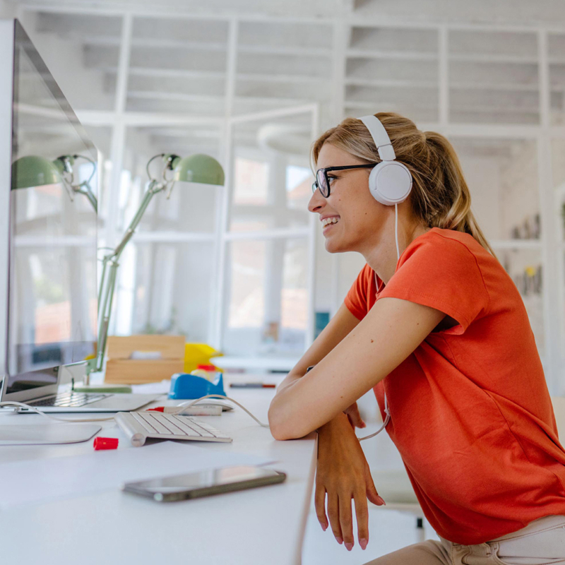 Frau in orangenem Shirt vor Laptop